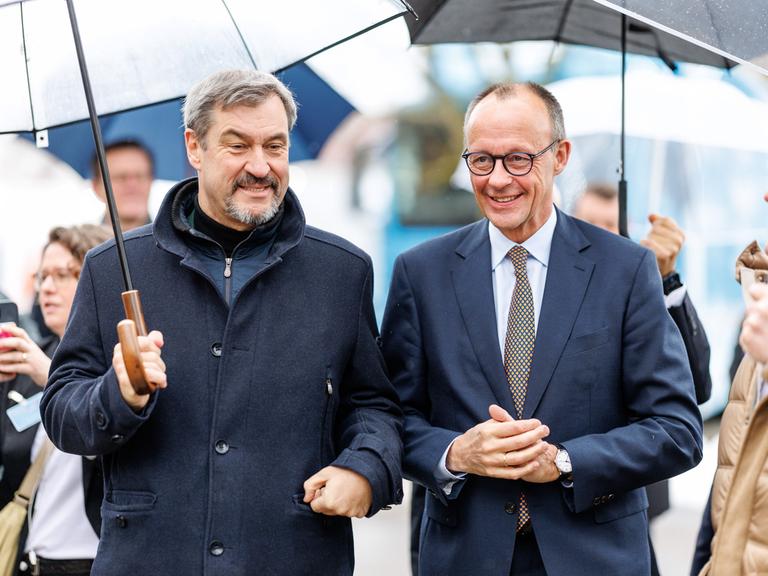 Markus Söder (CSU), Parteivorsitzender und Ministerpräsident von Bayern, und Friedrich Merz, Bundesvorsitzender der CDU und CDU-Kanzlerkandidat stehen nebeneinander unter Schirmen.