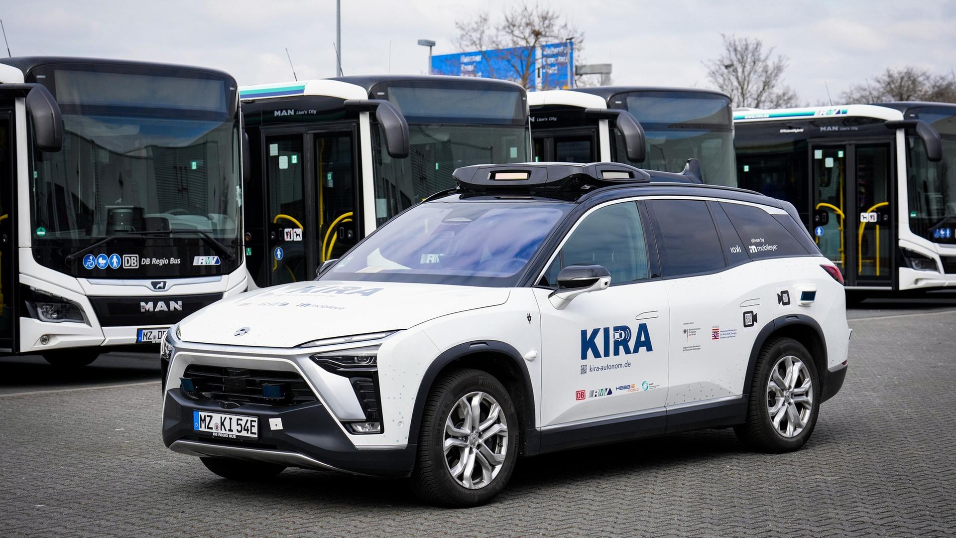 Ein selbstfahrender PKW steht vor einer Reihe von Linienbussen. Ein selbstfahrender PKW steht vor einer Reihe von Linienbussen.