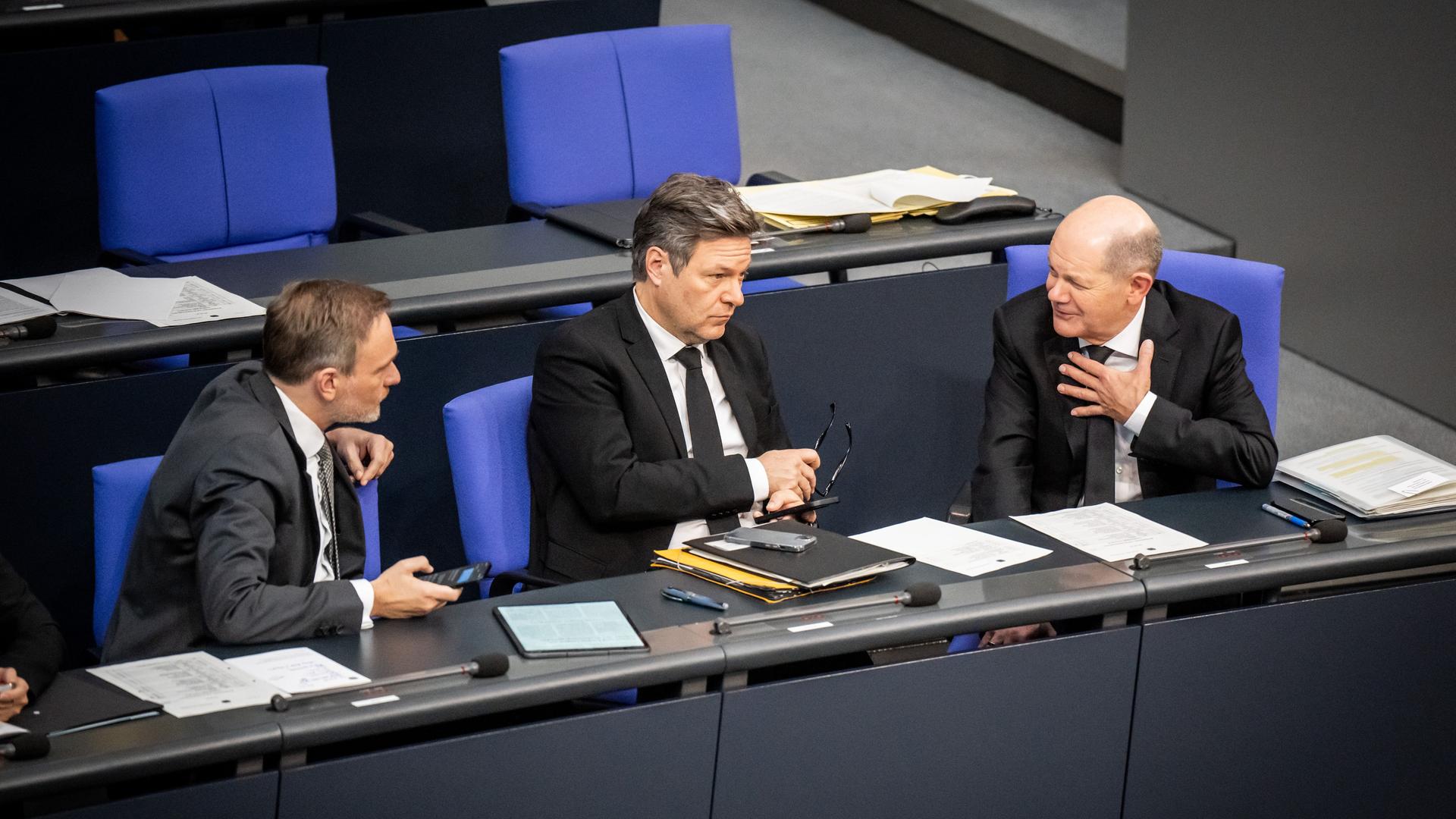 Christian Lindner, Olaf Scholz und Robert Habeck sitzen auf der Regierungsbank im Bundestag und unterhalten sich miteinander.