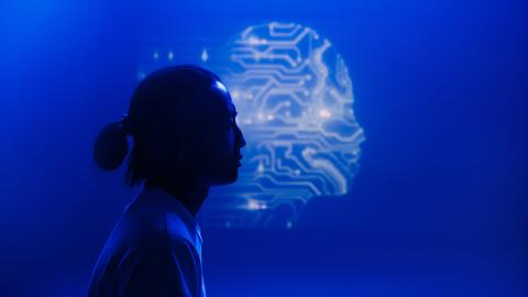 Eine menschliche Silhouette im Profil hebt sich vor dem Umriss eines Kopfes ab, der aus Schaltkreisen zu bestehen scheint.