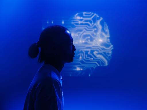 Eine menschliche Silhouette im Profil hebt sich vor dem Umriss eines Kopfes ab, der aus Schaltkreisen zu bestehen scheint.