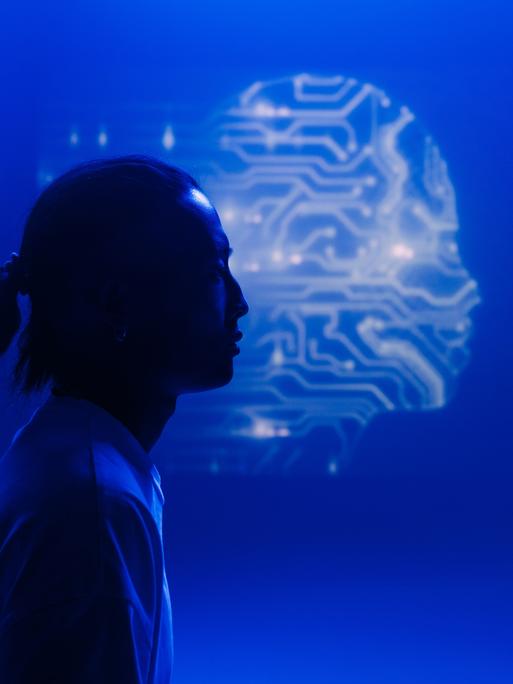 Eine menschliche Silhouette im Profil hebt sich vor dem Umriss eines Kopfes ab, der aus Schaltkreisen zu bestehen scheint.