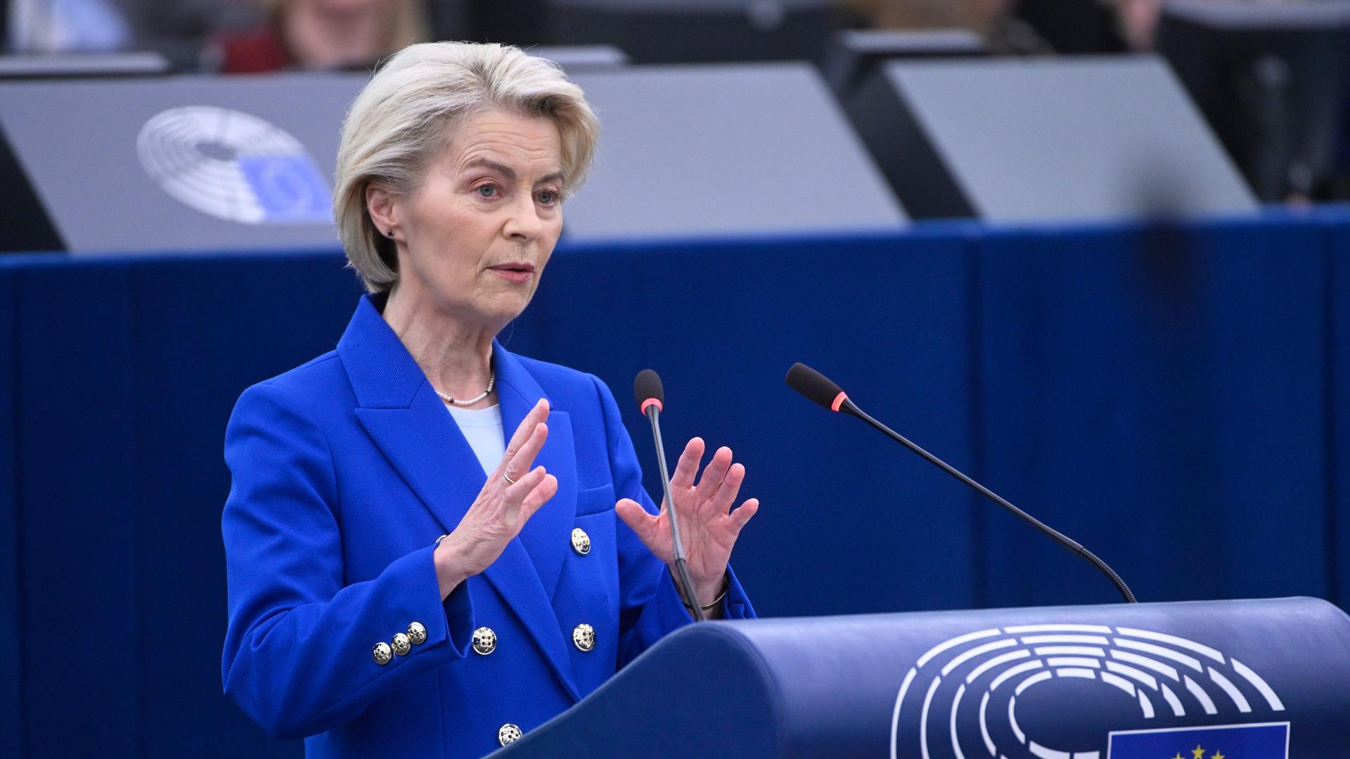 Von der Leyen im blauen Kostüm steht am Rednerpult, sagt etwas und gestikuliert dazu mit beiden Händen. 
