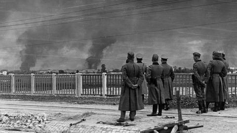 Im Vordergrund stehen deutsche Soldaten der Wehrmacht und beobachten die Angriffe auf Warschau.