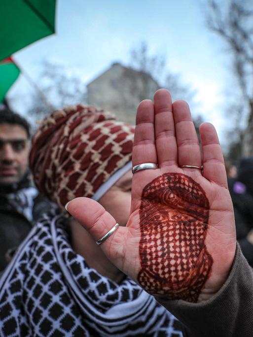 Eine Demonstrantin hält ihre Handfläche in die Kamera, auf die mit Henna das Porträt des toten Hamas-Sprechers Abu Obaida gezeichnet ist.