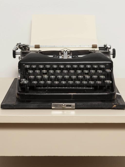 Eine schwarze, alte Schreibmaschine steht auf einem weißen Tisch.