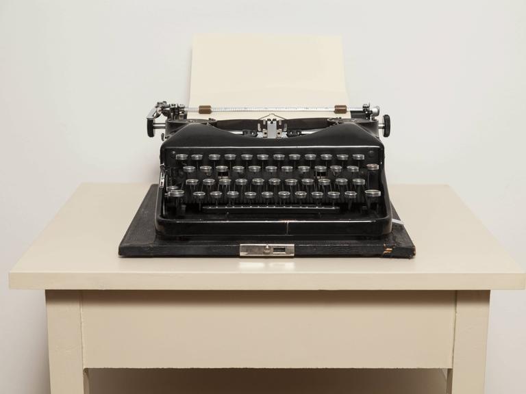 Eine schwarze, alte Schreibmaschine steht auf einem weißen Tisch.