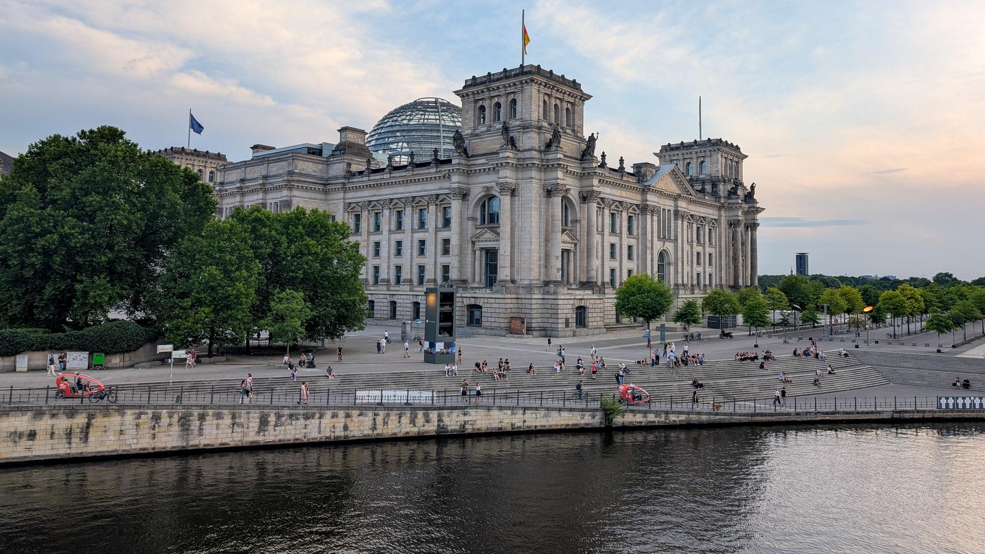 Das Reichstagsgebäude mit der Glaskuppel von der Seite. Davor ist die Spree zu sehen.