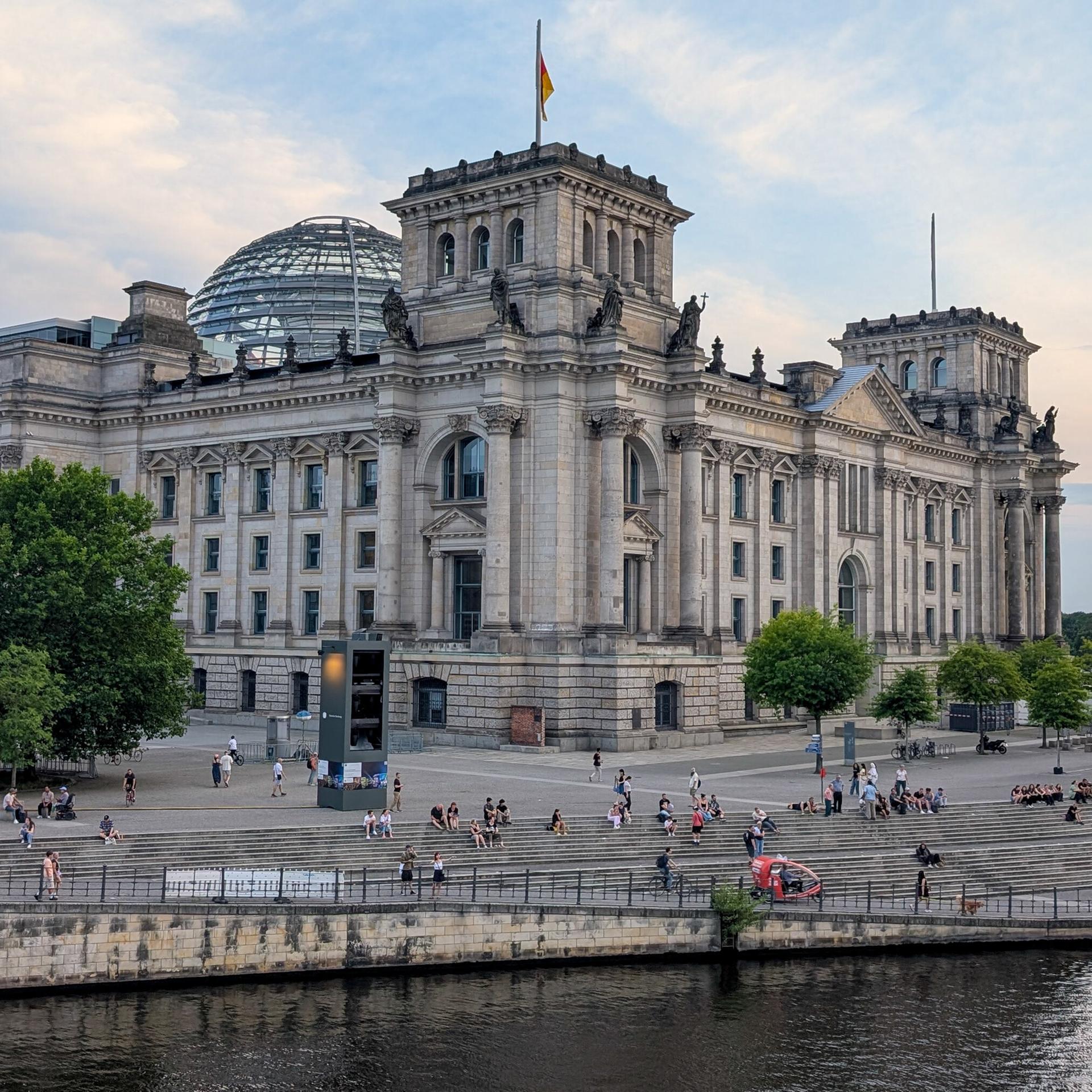 Das Reichstagsgebäude mit der Glaskuppel von der Seite. Davor ist die Spree zu sehen.