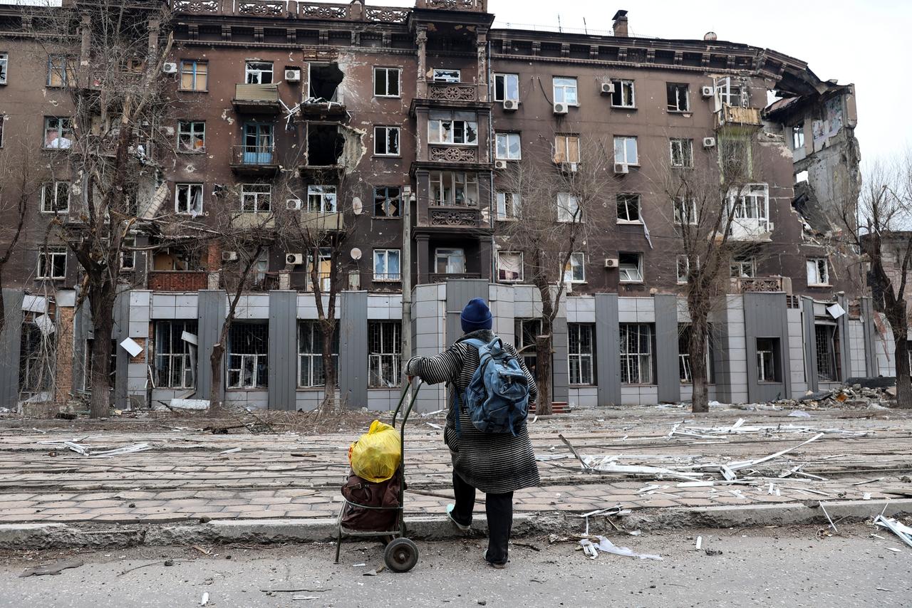 Eine Frau steht vor einem zerstörten Wohnhaus in der ukrainischen Hafenstadt Mariupol.