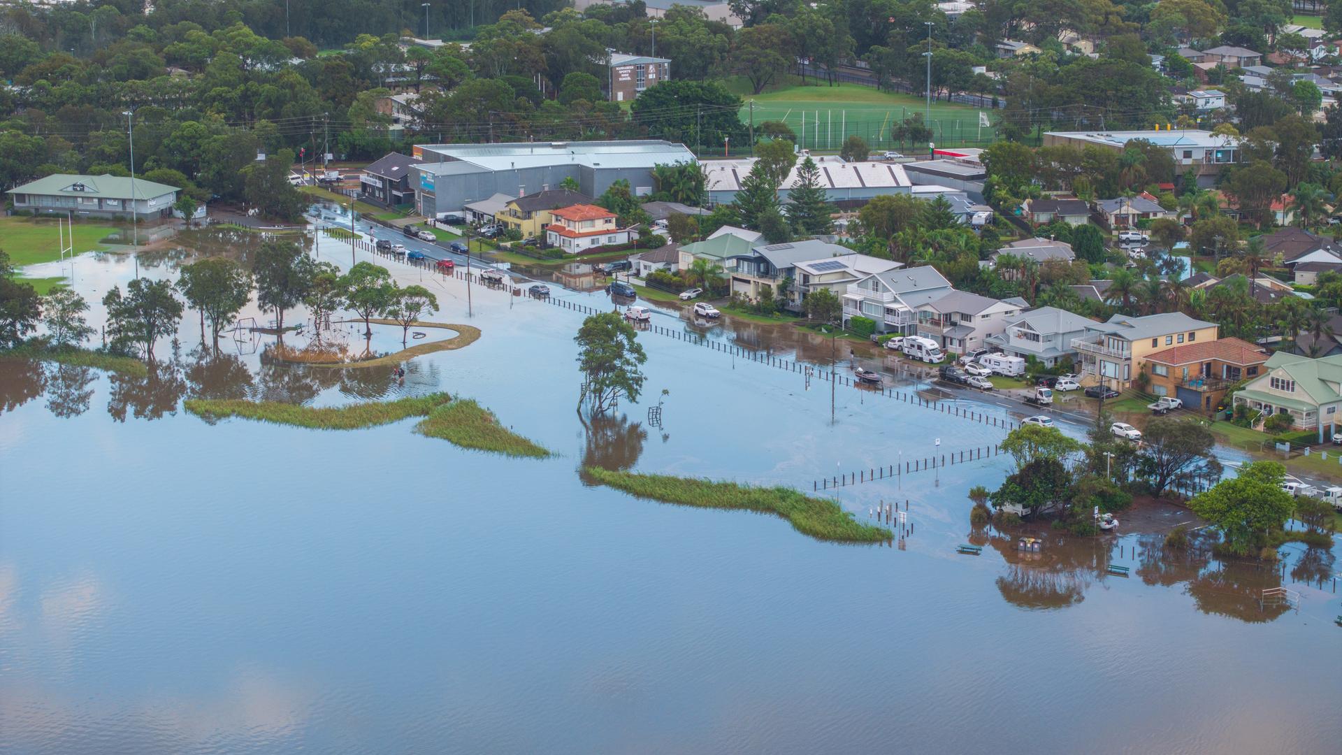Eine Wiese und eine Straße stehen in einem Vorort von Sydney unter Wasser. Dahinter befinden sich Wohnhäuser. Eine Wiese und eine Straße stehen in einem Vorort von Sydney unter Wasser. Dahinter befinden sich Wohnhäuser.