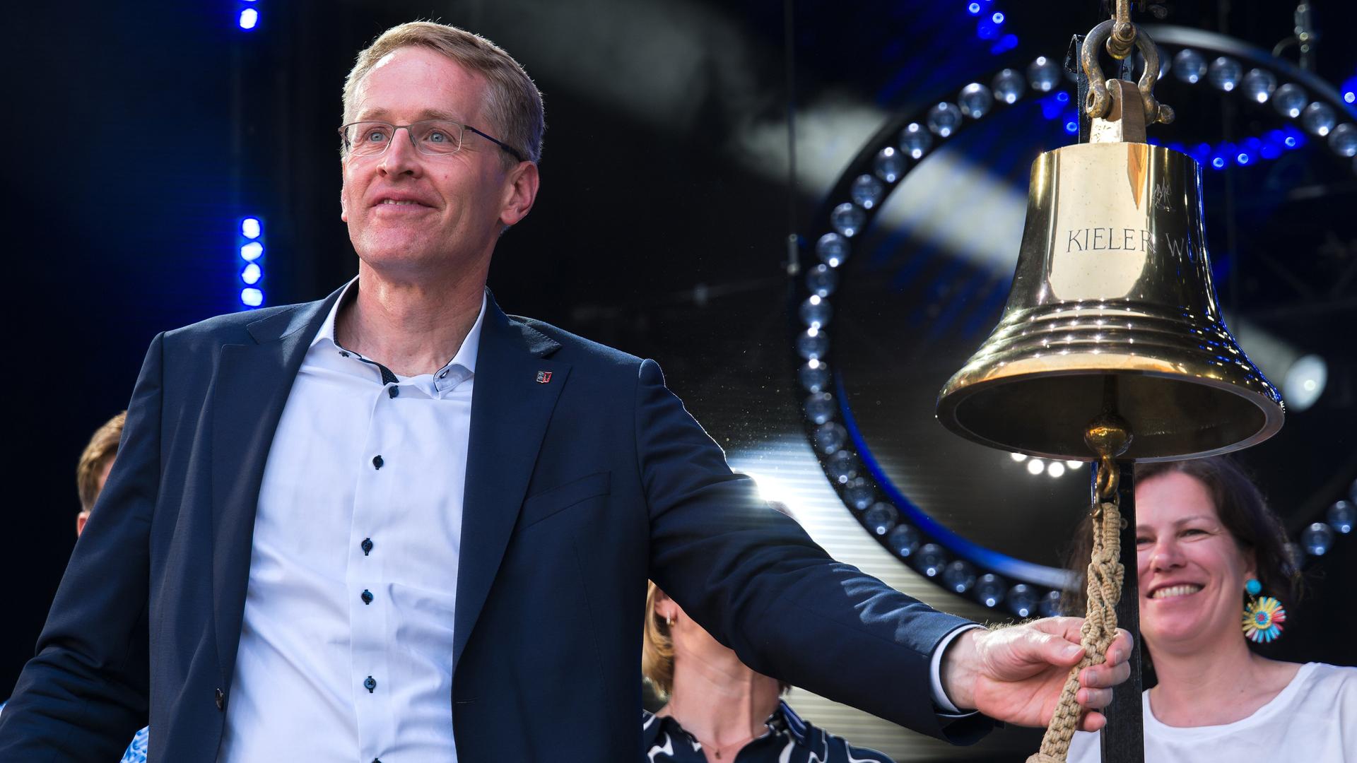 Daniel Günther läutet eine große, goldene Schiffsglocke mit der Aufschrift "Kieler Woche". Daniel Günther läutet eine große, goldene Schiffsglocke mit der Aufschrift "Kieler Woche".