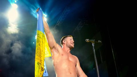 Frontmann Dan Reynolds steht halbnackt auf einer erleuchteten Bühne und hält eine Fahne der Ukraine hoch und animiert seine Fans.