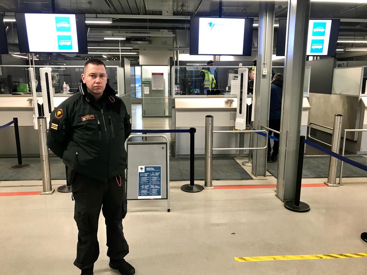 Jussi Pekkola trägt eine schwarze Sicherheitsuniform und steht in dem Grenzhaus vor dem Sicherheitkontrollen-Bereich.