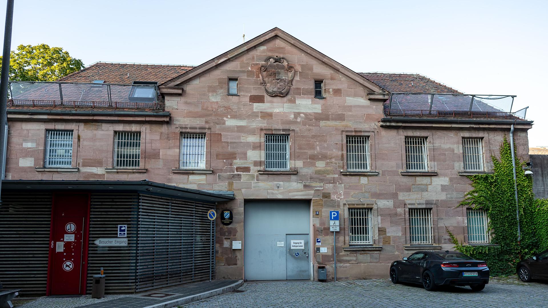 Das Bild zeigt die Vorderansicht eines Gebäudes der Justizvollzugsanstalt Nürnberg. Das Gebäude ist aus Sandstein gebaut und mit vergitterten Fenstern versehen. 