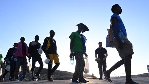 Flüchtlinge, die auf der Insel Lampedusa ankommen und in der Sonne laufen während sie von der Polizei beobachtet werden.