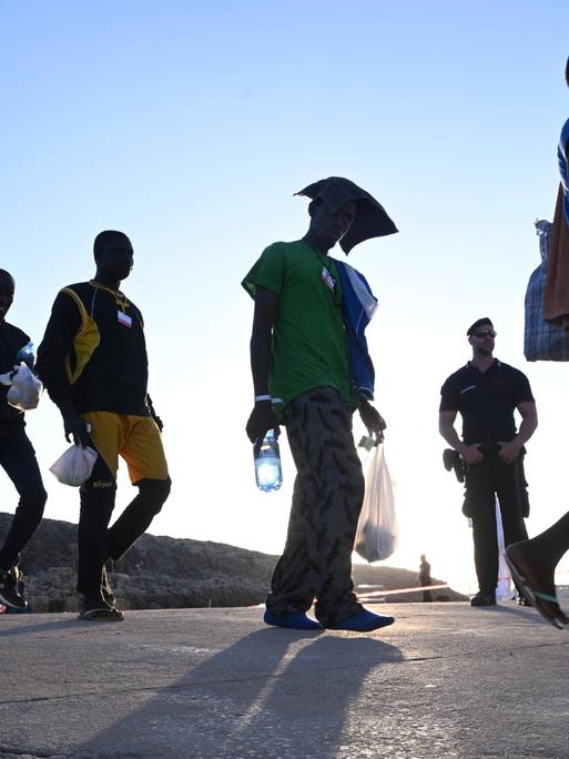 Flüchtlinge, die auf der Insel Lampedusa ankommen und in der Sonne laufen während sie von der Polizei beobachtet werden. 