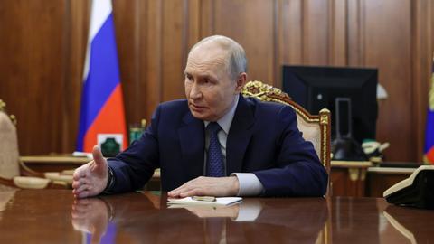 Russlands Präsident Wladimir Putin sitzt an seinem Schreibtisch und macht eine Handbewegung