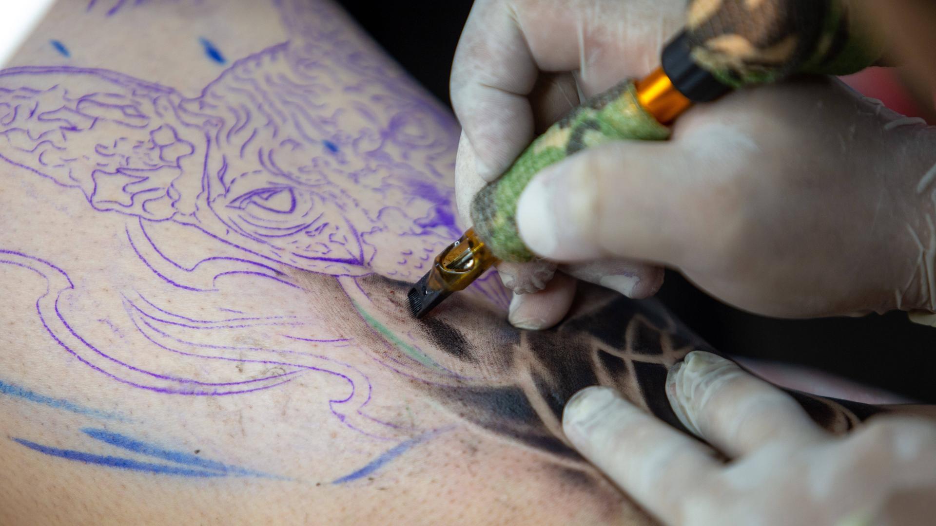 Ein Tätowierer sticht ein Tattoo Ein Tätowierer sticht ein Tattoo