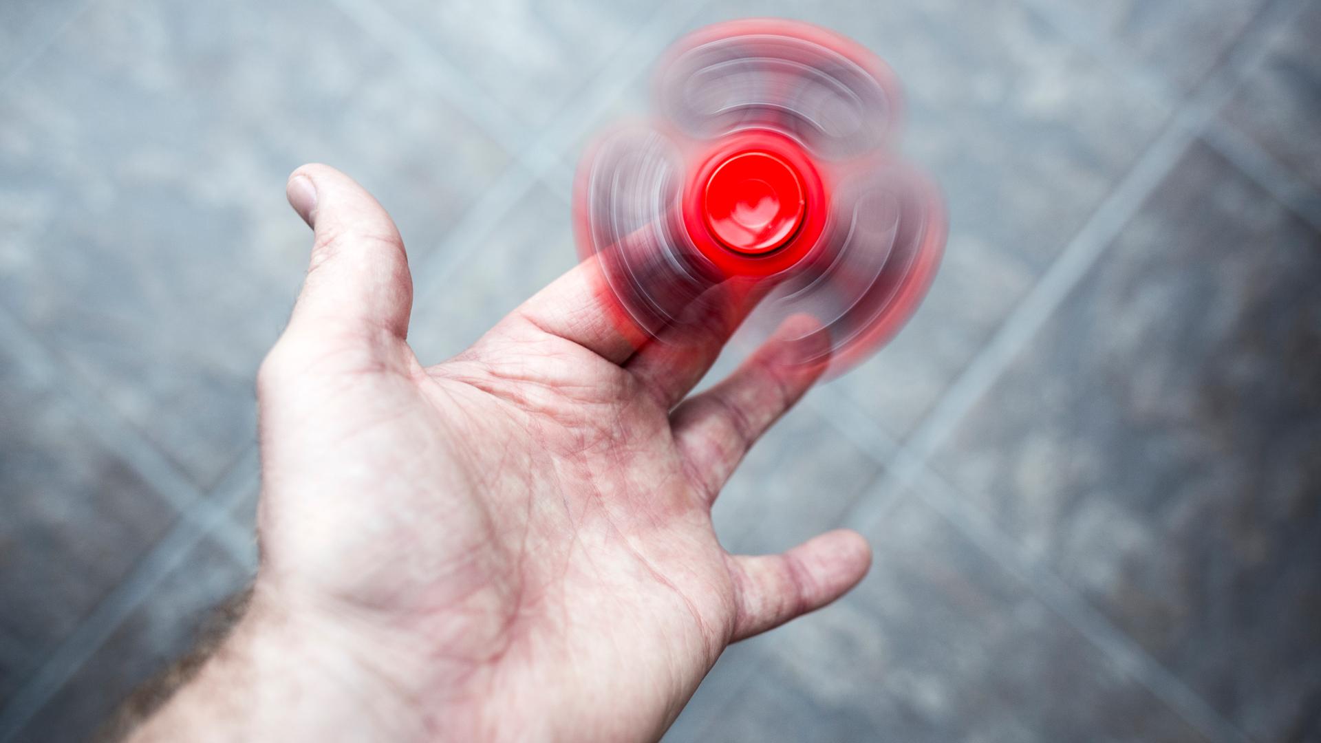 Ein roter Figest Spinner dreht sich schnell in der Hand einer erwachsenen Person.