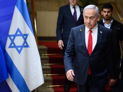 Benjamin Netanjahu, Ministerpräsident von Israel, läuft eine Treppe hinunter, ein Personenschützer ist hinter zu sehen. Neben ihm ist die Flagge Israels zu erkennen.