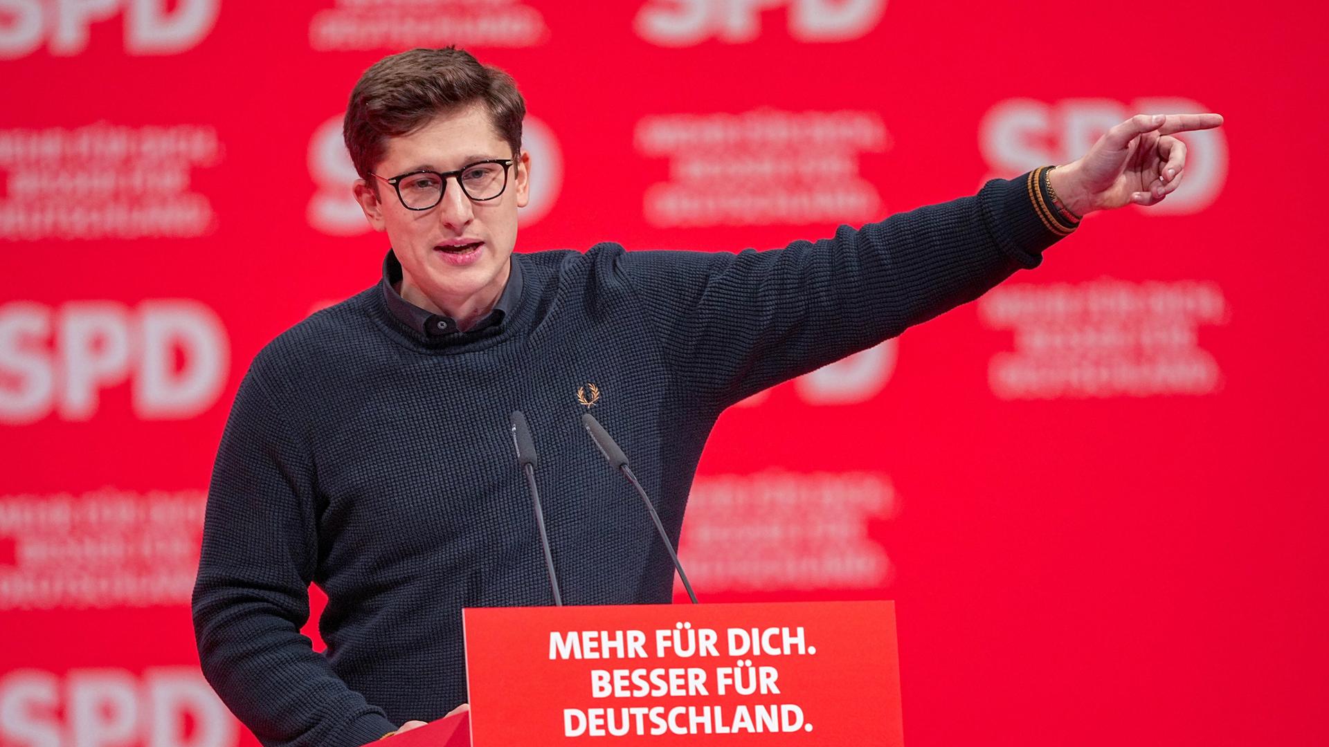 Philipp Türmer (SPD), Bundesvorsitzender der SPD-Jugendorganisation Jusos, steht beim SPD-Bundesparteitag am Rednerpult, spricht und zeigt mit dem Arm und Zeigefinger nach links. 
