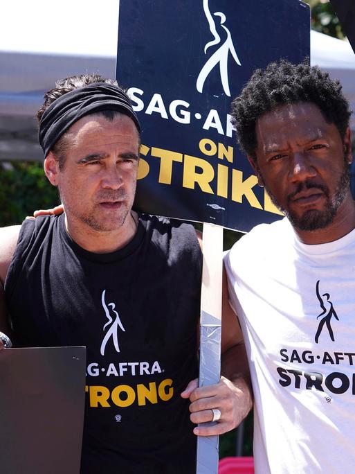Drei US-Schauspieler beim Streikmarsch in Hollywood. Sie halten Plakate mit dem Namen der Schauspielergewerkschaft SAG-AFTRA hoch.