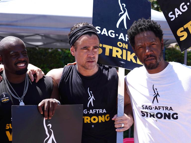 Drei US-Schauspieler beim Streikmarsch in Hollywood. Sie halten Plakate mit dem Namen der Schauspielergewerkschaft SAG-AFTRA hoch.