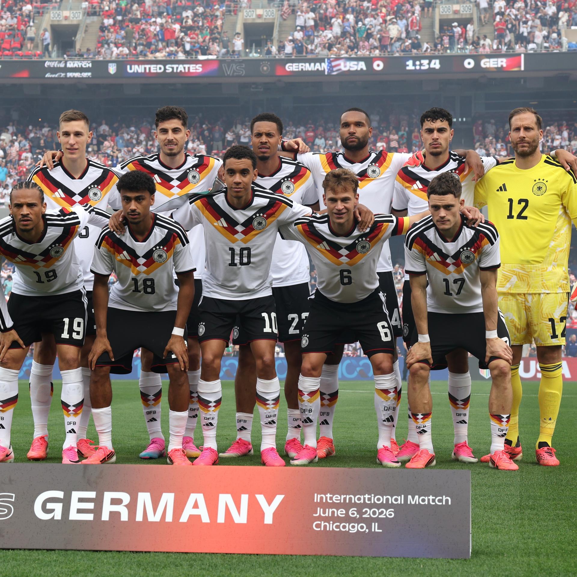 Mannschaftfoto des Teams: Die Spieler stehen in zwei Reihen vor einer vollbesetzten Trinübe auf dem Rasen. 
