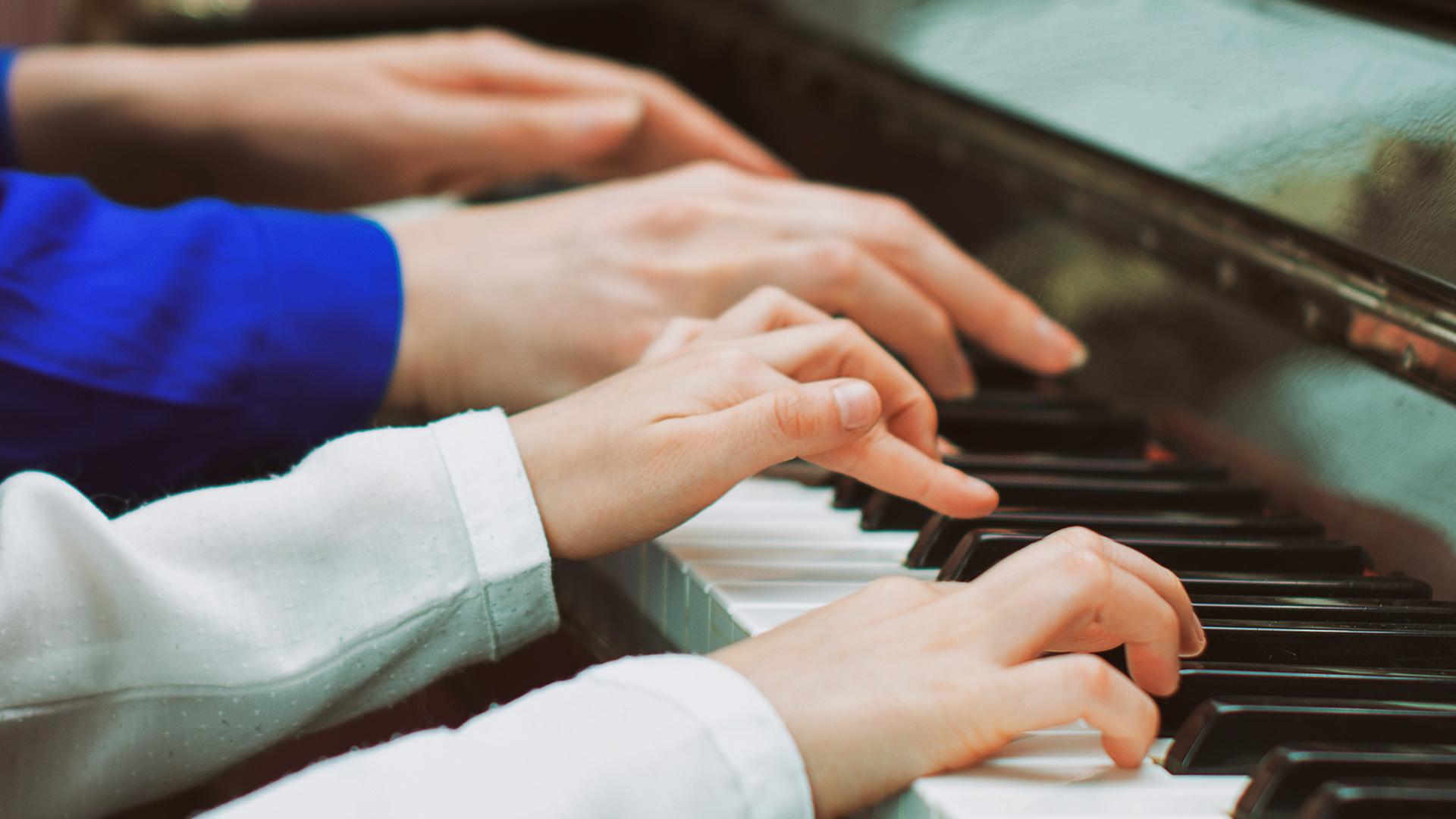Vier Hande auf einer Klaviertastatur, die kleinen Hände eines Kindes und die Hände einer Klavierlehrerin.