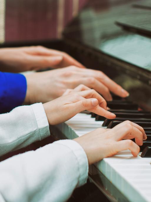 Vier Hande auf einer Klaviertastatur, die kleinen Hände eines Kindes und die Hände einer Klavierlehrerin.