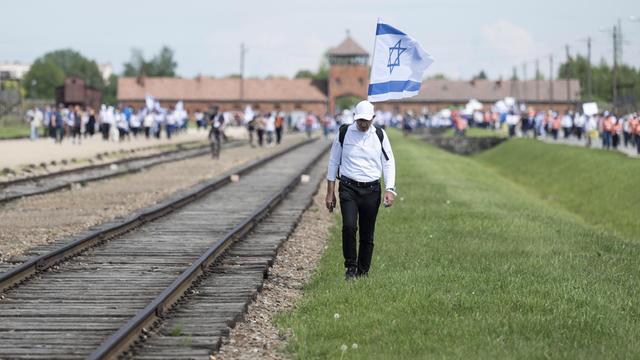 Ein Mann mit einer großen Flagge läuft neben Bahnschienen. Auf der Flagge ist ein blauer Stern.