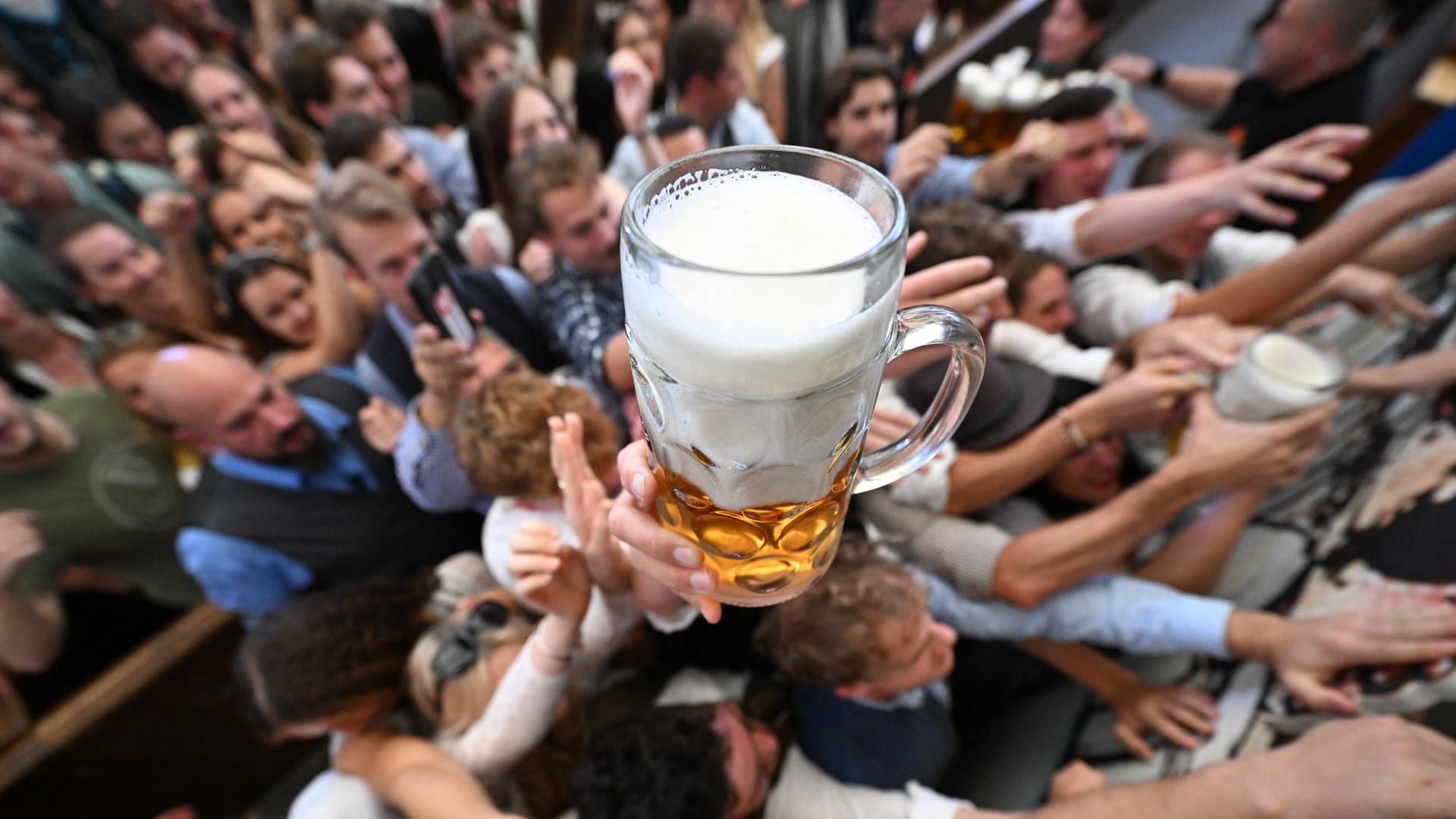 Ein großer Bierkrug schwebt über den Besuchern des Münchner Oktoberfests. Hände recken sich nach oben. 