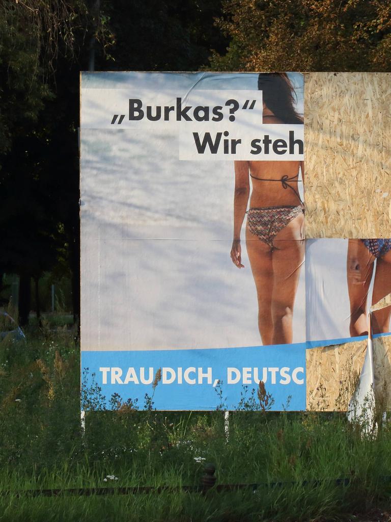Teilweise zerstörtes Wahlplakat der AfD, auf dem zwei Frauen von hinten zu sehen sind. Sie tragen beide Bikinis. Die Aufschrift beginnt mit "Burkas? Wir steh". Weiter ist es nicht zu lesen.