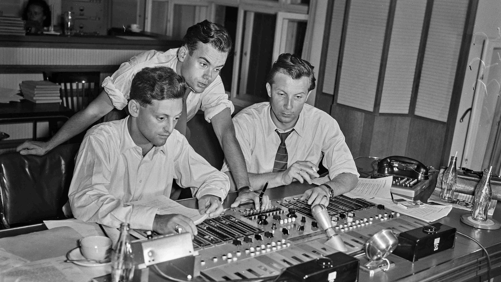 Schwarz-weiß Aufnahme von drei jungen Männern vor einem Mischpult in einem Studio in den 60er-Jahren.