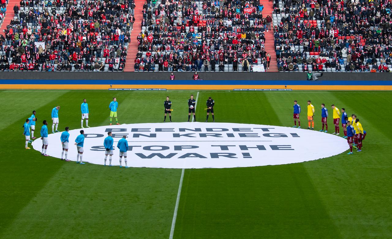 Die Spieler von München und von Leverkusen stehen vor dem Spiel um ein Banner mit der Aufschrift "Beendet den Krieg! - Stop the War!" zusammen. 