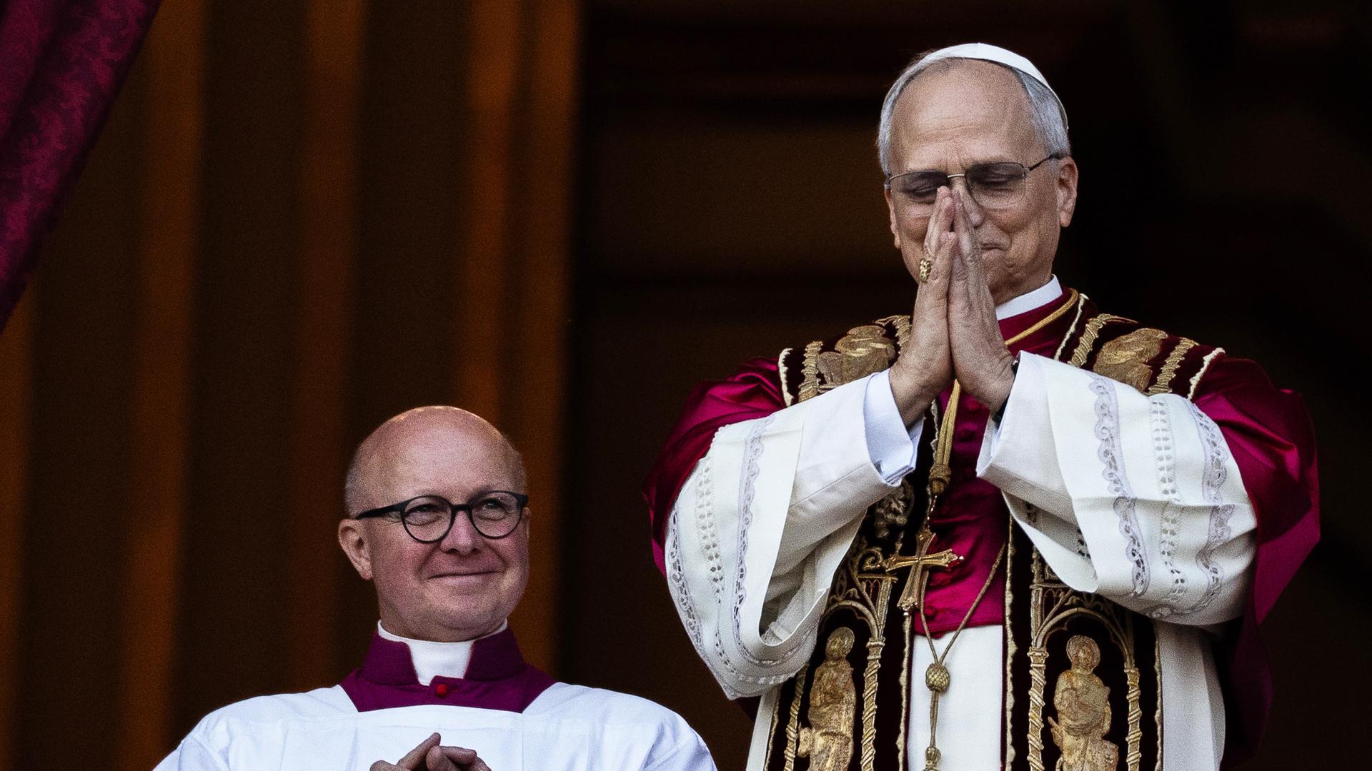 Der neu gewählte Papst Leo XIV. (r) steht mit gefalteten Händen auf dem Balkon des Petersdoms im Vatikan. Der neu gewählte Papst Leo XIV. (r) steht mit gefalteten Händen auf dem Balkon des Petersdoms im Vatikan.