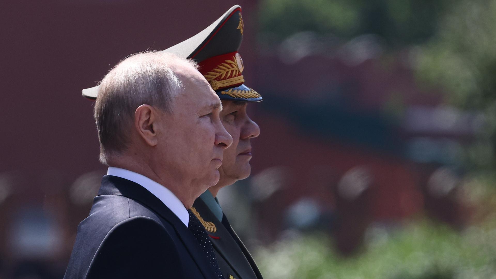 Wladimir Putin (vorn) und der russische Verteidigungsminister Shoigu (hinten) stehen Seite an Seite und blicken ernst in die Ferne.