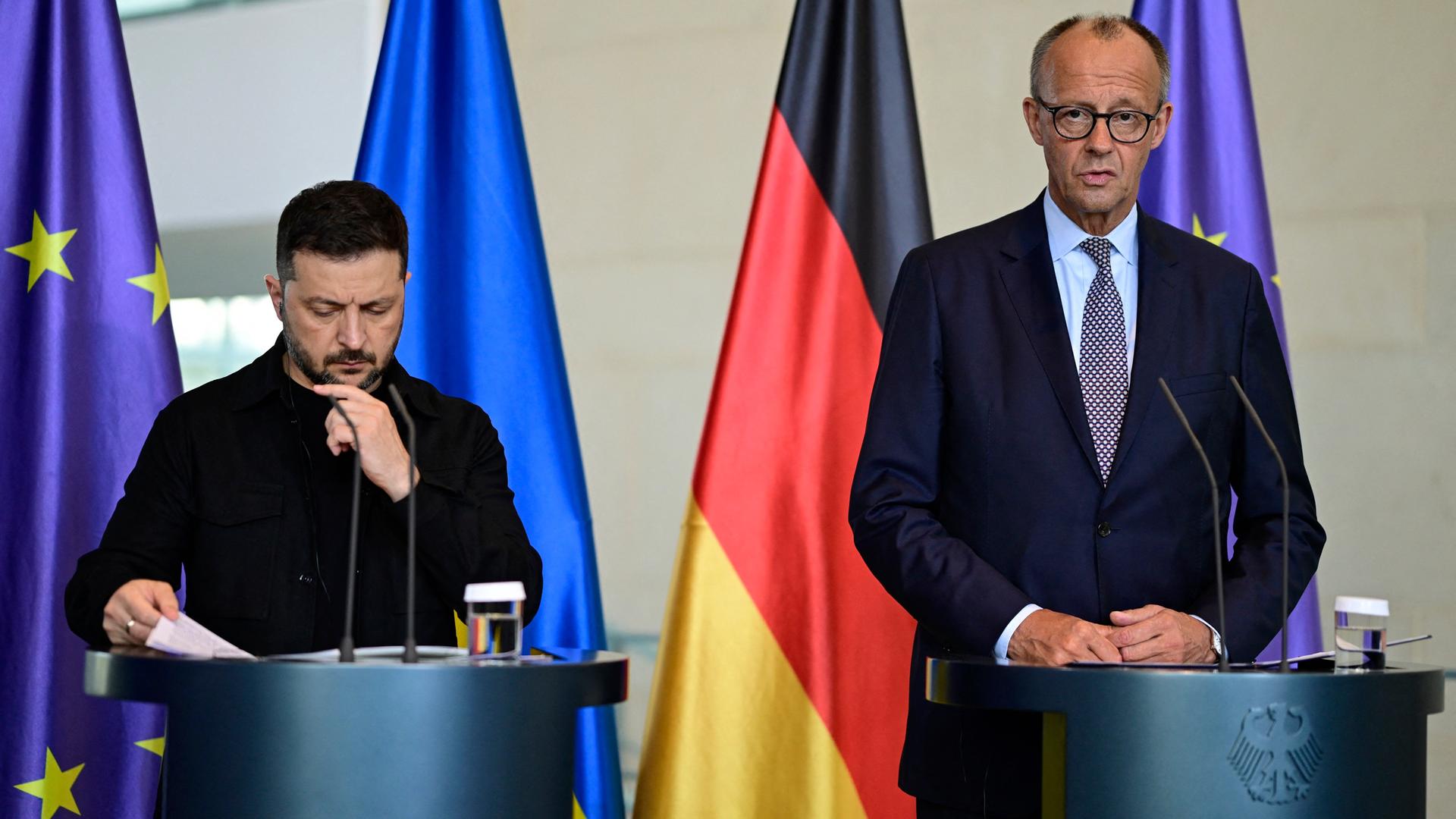 Die beiden stehen nebeneinander an Rednerpulten vor den Fahen ihrer Staaten und der EU-Flagge. Merz spricht gerade. Die beiden stehen nebeneinander an Rednerpulten vor den Fahen ihrer Staaten und der EU-Flagge. Merz spricht gerade.