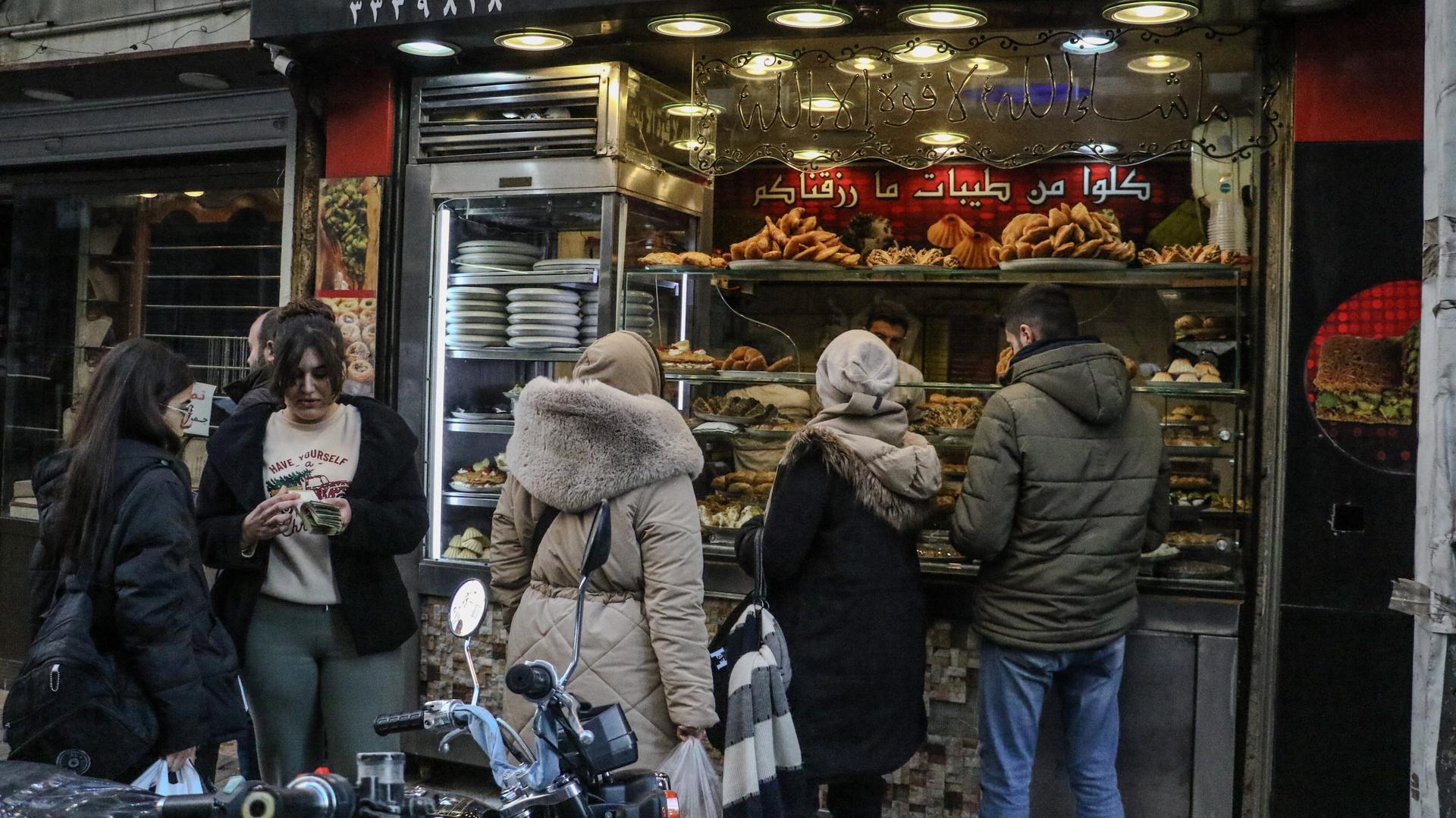 Vier Frauen und ein Mann stehen vor einem Geschäft in der syrischen Hauptstadt Damaskus. Eine Frau schaut auf ihr Smartphone. Zwei tragen Kopftuch, zwei nicht.