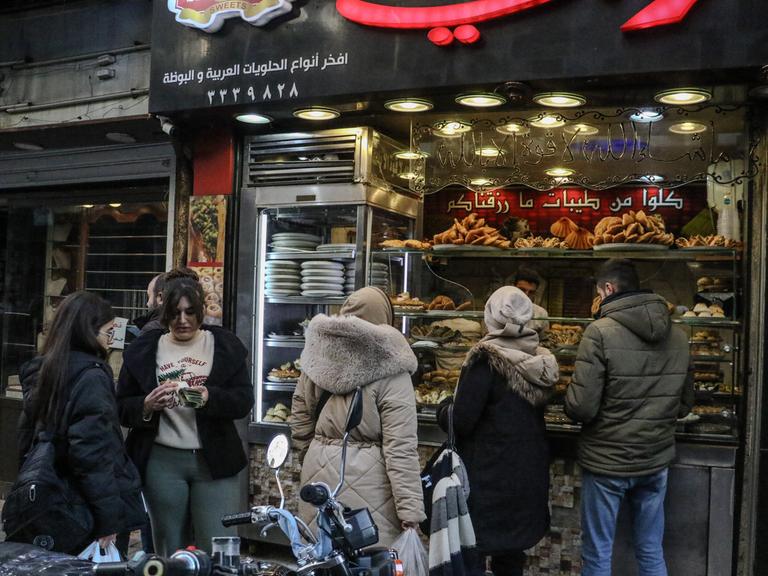 Vier Frauen und ein Mann stehen vor einem Geschäft in der syrischen Hauptstadt Damaskus. Eine Frau schaut auf ihr Smartphone. Zwei tragen Kopftuch, zwei nicht.