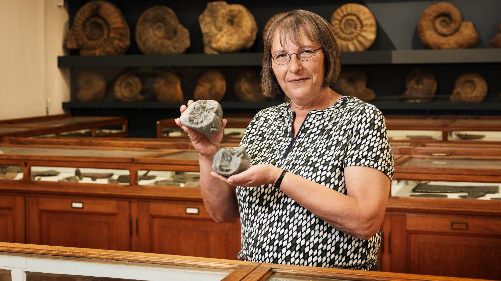 Die Paläontologin Madelaine Böhme steht vor einem Regal mit Fossilien. Sie hält vergrößerte 3D-Modelle von Backenzähnen von Menschenaffen.