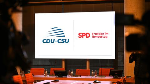 Unbesetzte Stühle sind zwischen Kameras vor einem Bildschirm mit den Logos von CDU/CSU und SPD in einem Tagungsraum im Jakob-Kaiser-Haus zu sehen. 