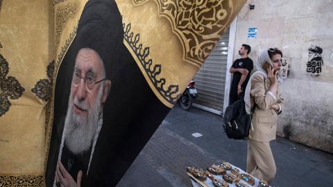 Alltag im Iran. Eine Frau geht in Teheran an einer Flagge mit dem Porträt des bei Luftangriffen der USA und Israels getöteten geistlichen Führers Ayatollah Ali Chamenei vorbei