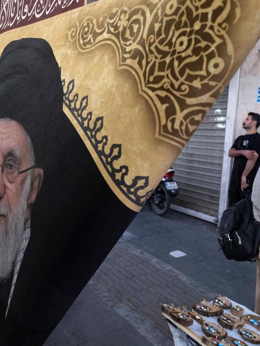 Alltag im Iran. Eine Frau geht in Teheran an einer Flagge mit dem Porträt des bei Luftangriffen der USA und Israels getöteten geistlichen Führers Ayatollah Ali Chamenei vorbei
