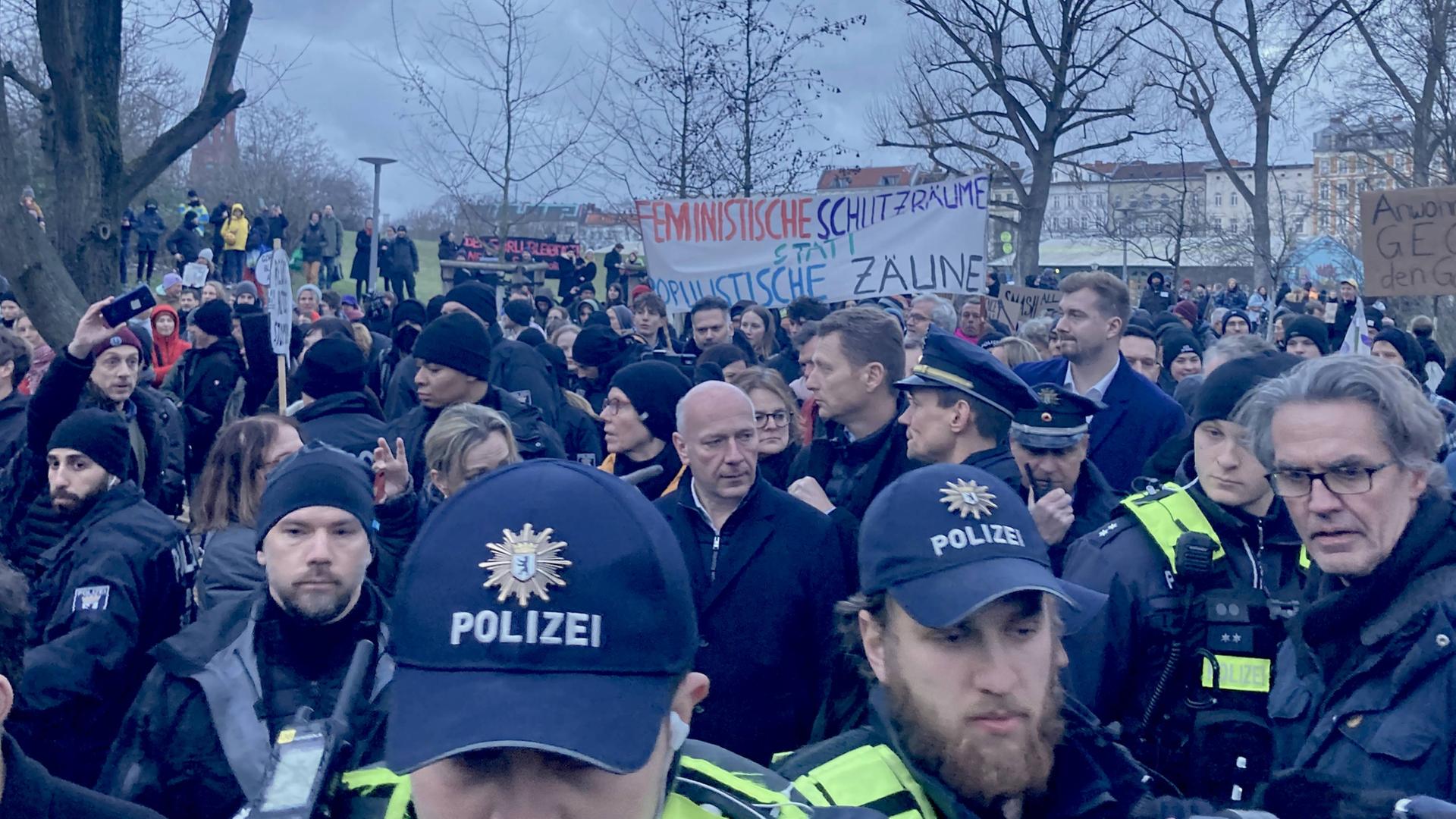 Demo im Görlitzer Park: Berlins Regierdender Bürgermeister Kai Wegner steht in einer Menge zwischen Polizei und Demonstrierenden. Im Hintergrund ein Banner mit der Aufschrift "Feministische Schutzräume statt populistische Zäune". Demo im Görlitzer Park: Berlins Regierdender Bürgermeister Kai Wegner steht in einer Menge zwischen Polizei und Demonstrierenden. Im Hintergrund ein Banner mit der Aufschrift "Feministische Schutzräume statt populistische Zäune".