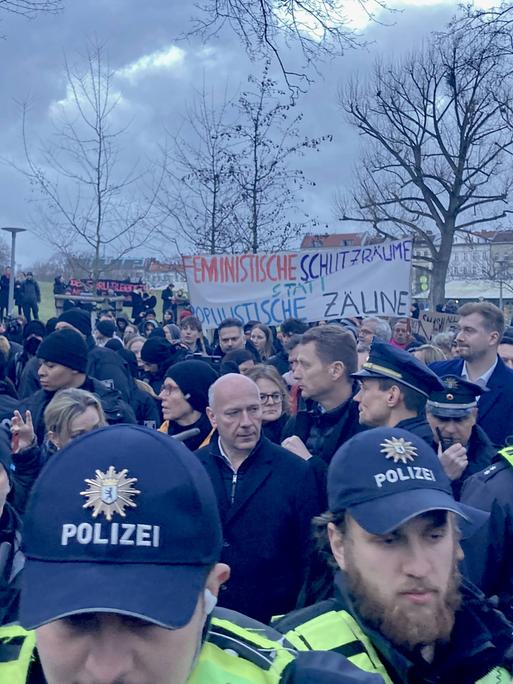 Demo im Görlitzer Park: Berlins Regierdender Bürgermeister Kai Wegner steht in einer Menge zwischen Polizei und Demonstrierenden. Im Hintergrund ein Banner mit der Aufschrift "Feministische Schutzräume statt populistische Zäune".