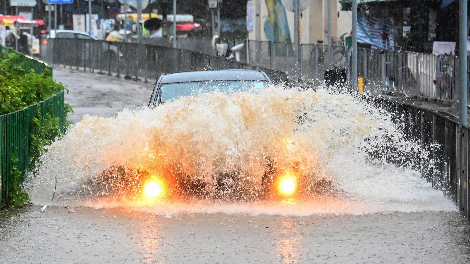 Ein Auto fährt in Hongkong durch eine überflutete Straße, das Wasser spritzt weit über die Scheinwerfern hinauf.