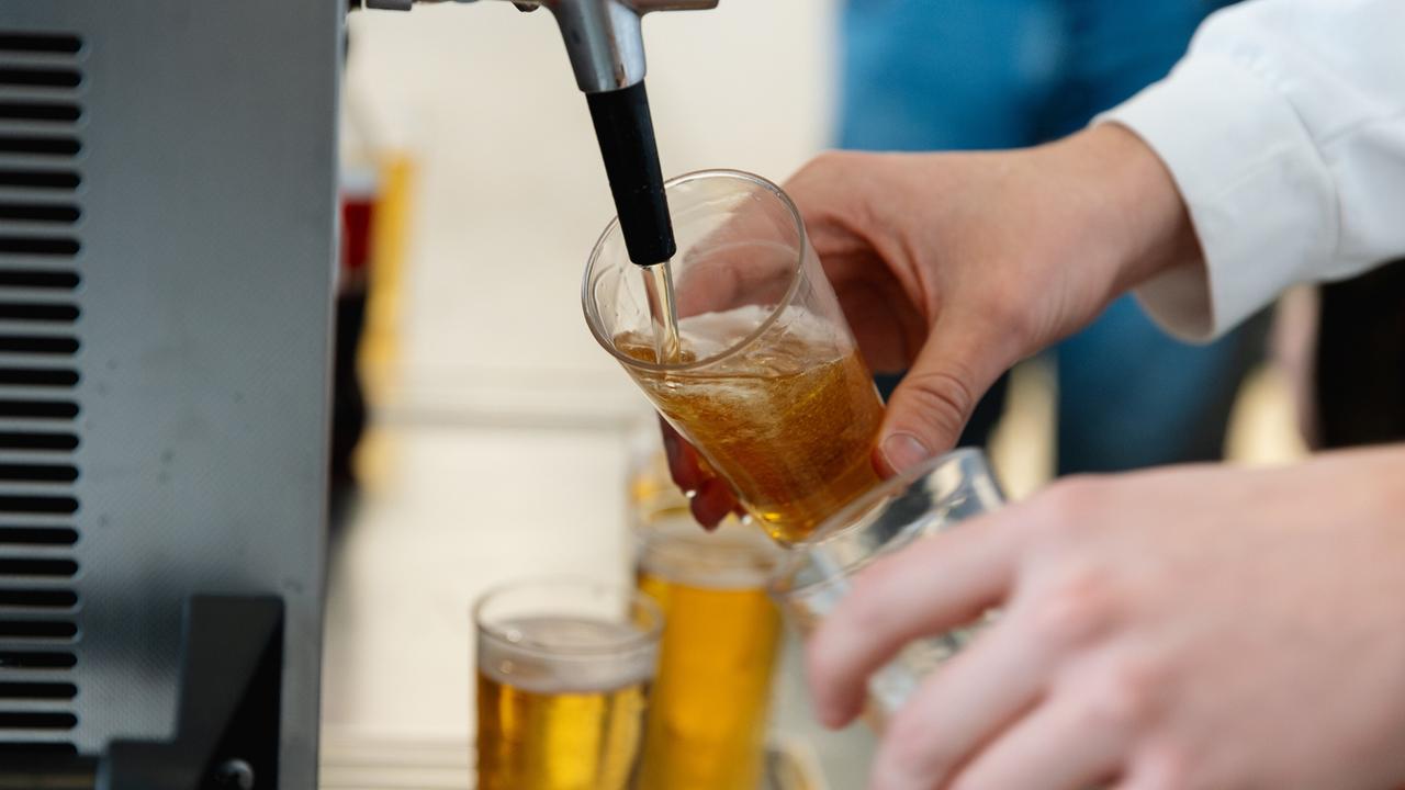 Nahaufnahme einer Person, die an einem Zapfhahn Bier in ein Glas füllt.