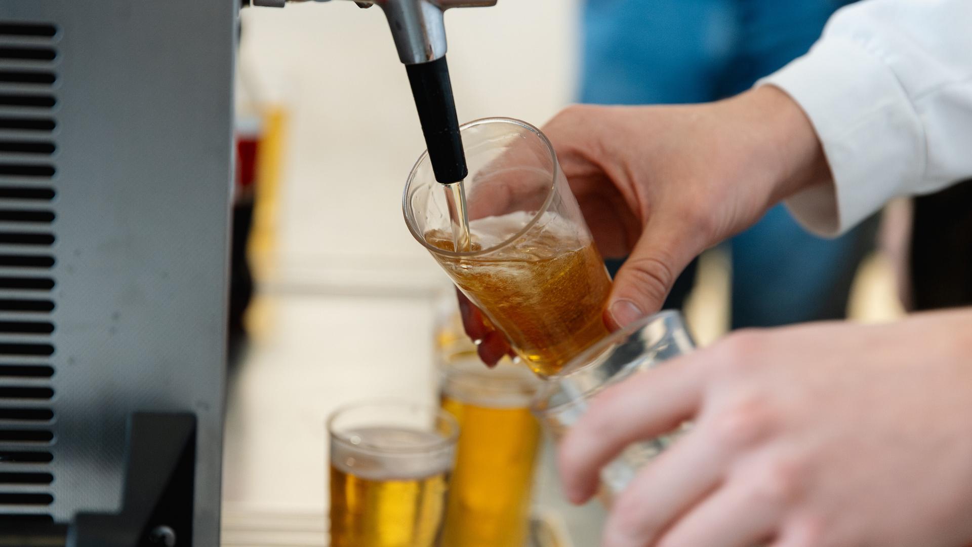 Nahaufnahme einer Person, die an einem Zapfhahn Bier in ein Glas füllt.